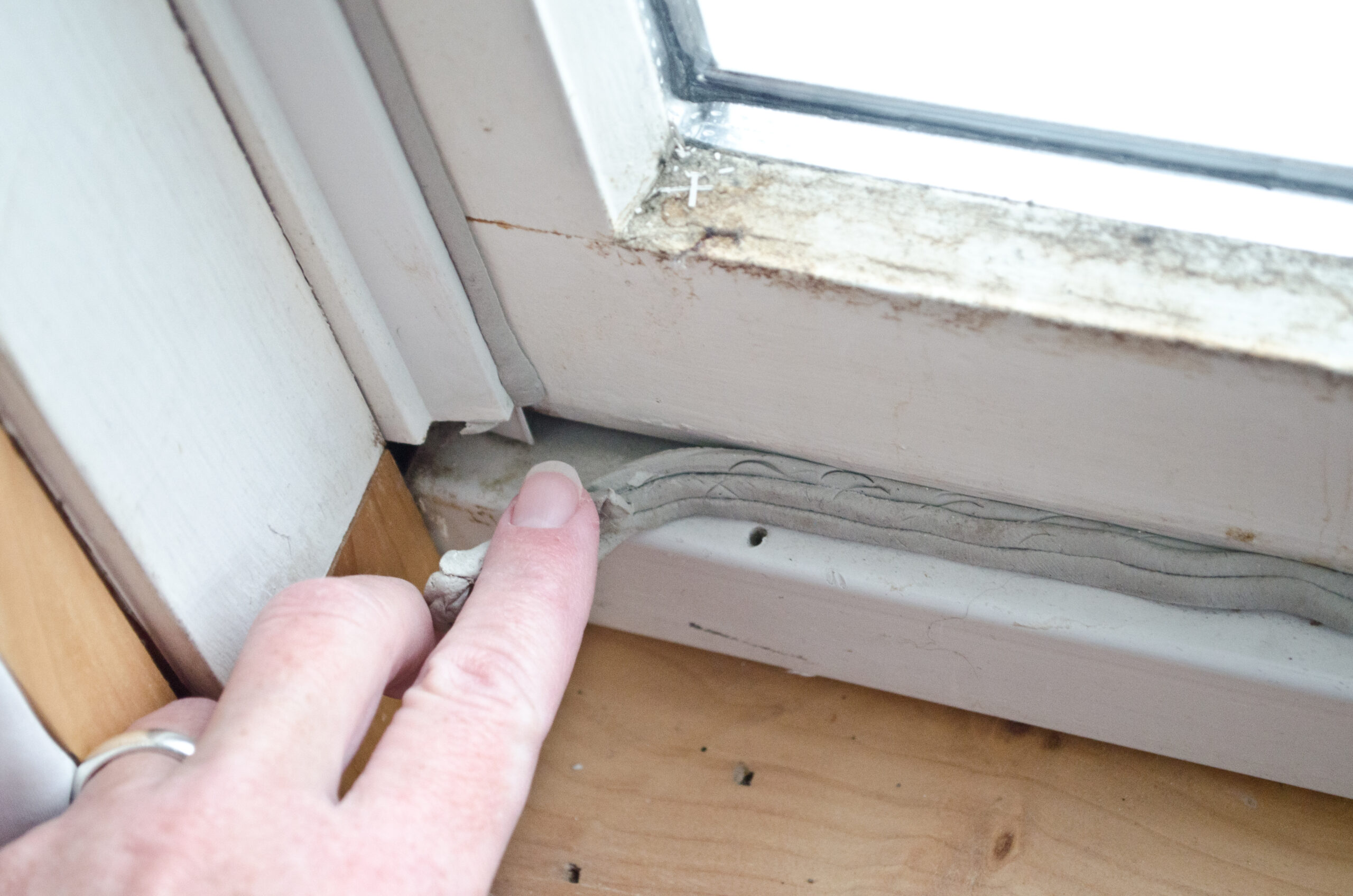 hand pressing in grey caulk in old window casement with bare wood windowsill for winterizing to keep out cold drafts and keep energy costs and heating bill down.